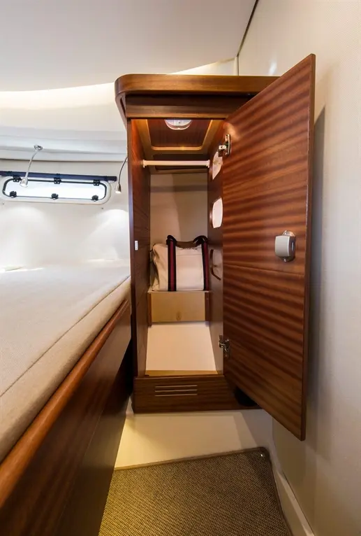 Interior of a yacht cabin featuring a wooden storage cabinet with an open door, revealing a bag inside.